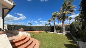 A well-maintained outdoor area with a curved brick pathway leading to a seating area, surrounded by lush greenery and palm trees. - Villa Amos Marzamemi San Lorenzo (San Lorenzo)