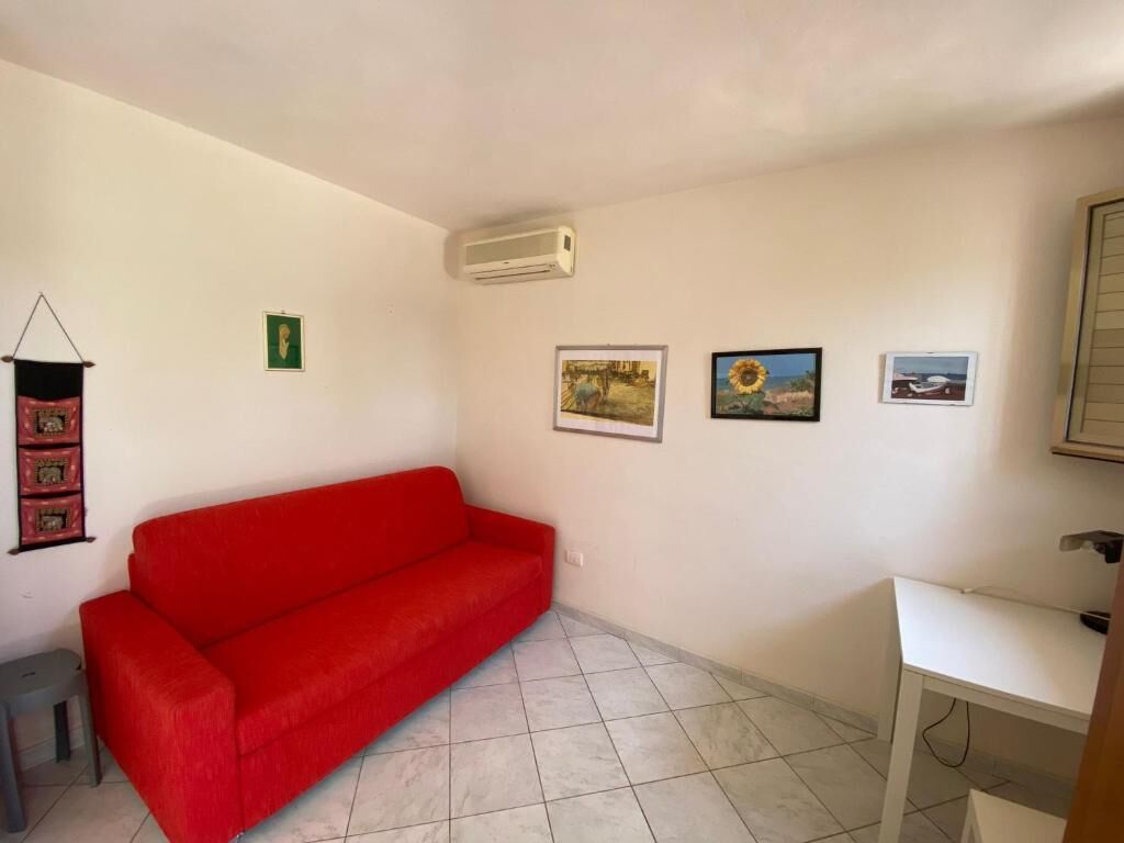 A room with a red sofa, a white desk, and several framed pictures on the wall.