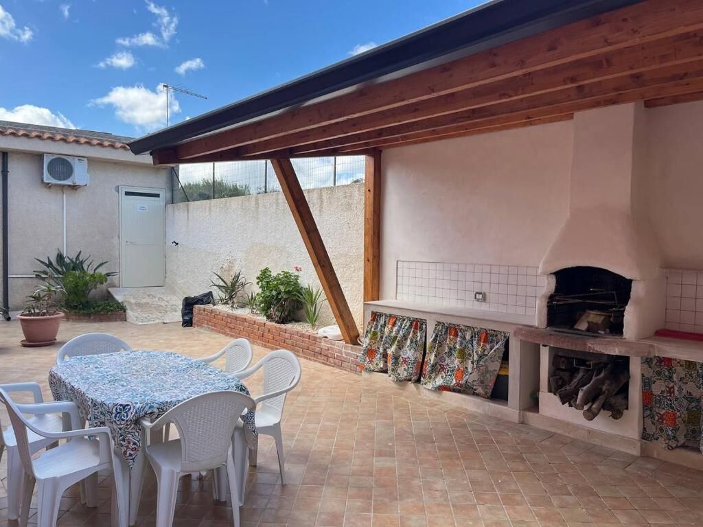 Une terrasse extérieure avec une table et des chaises, un mur en briques et une cheminée recouverte de carreaux.