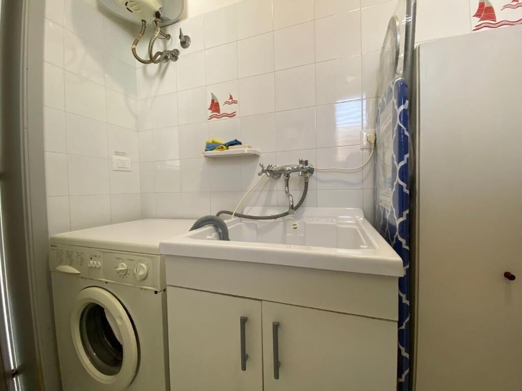 A compact laundry area with a washing machine, a sink, and a small shelf with toiletries.