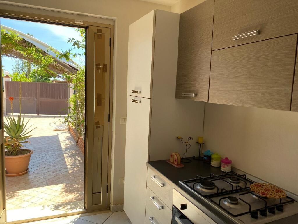 A kitchen with a gas stove, cabinets, and a sliding glass door leading to a patio with potted plants.