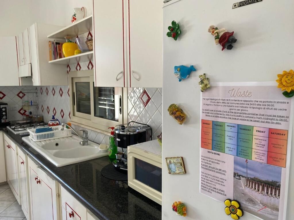 A kitchen with white cabinets, a black countertop, a sink, a microwave, and a refrigerator with magnets.