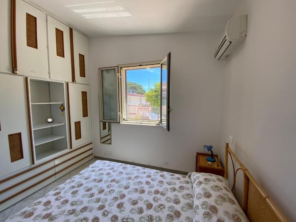 Un dormitorio con cama, armario, ventana y mesita de noche.