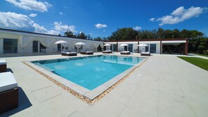 Un espace piscine extérieur moderne, avec un ciel bleu dégagé, entouré de chaises longues et de parasols.
