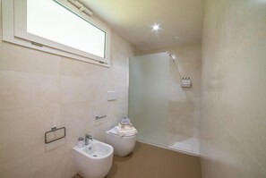 A modern bathroom with a bidet, a toilet, a glass shower enclosure, and a window above the bidet. - Agricola Chiani 1 Triple Relax&pool (Melendugno)