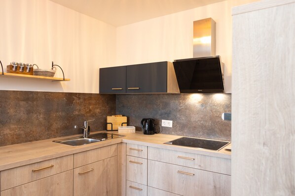 A modern kitchen with light wood cabinets, stainless steel appliances, and a built-in oven.