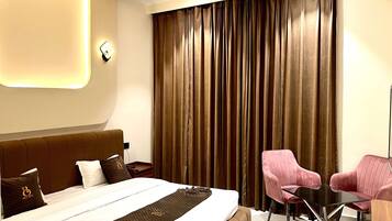 A modern hotel room with a large bed, a desk, and two pink chairs.