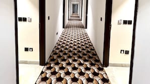 A long, narrow hallway with a patterned floor, white walls, and doors on both sides. - Hotel Bella Costa (Ludhiana)