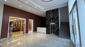 A lobby with a marble floor, a reception desk, a staircase, and a decorative floral archway. - Hotel Bella Costa (Ludhiana)