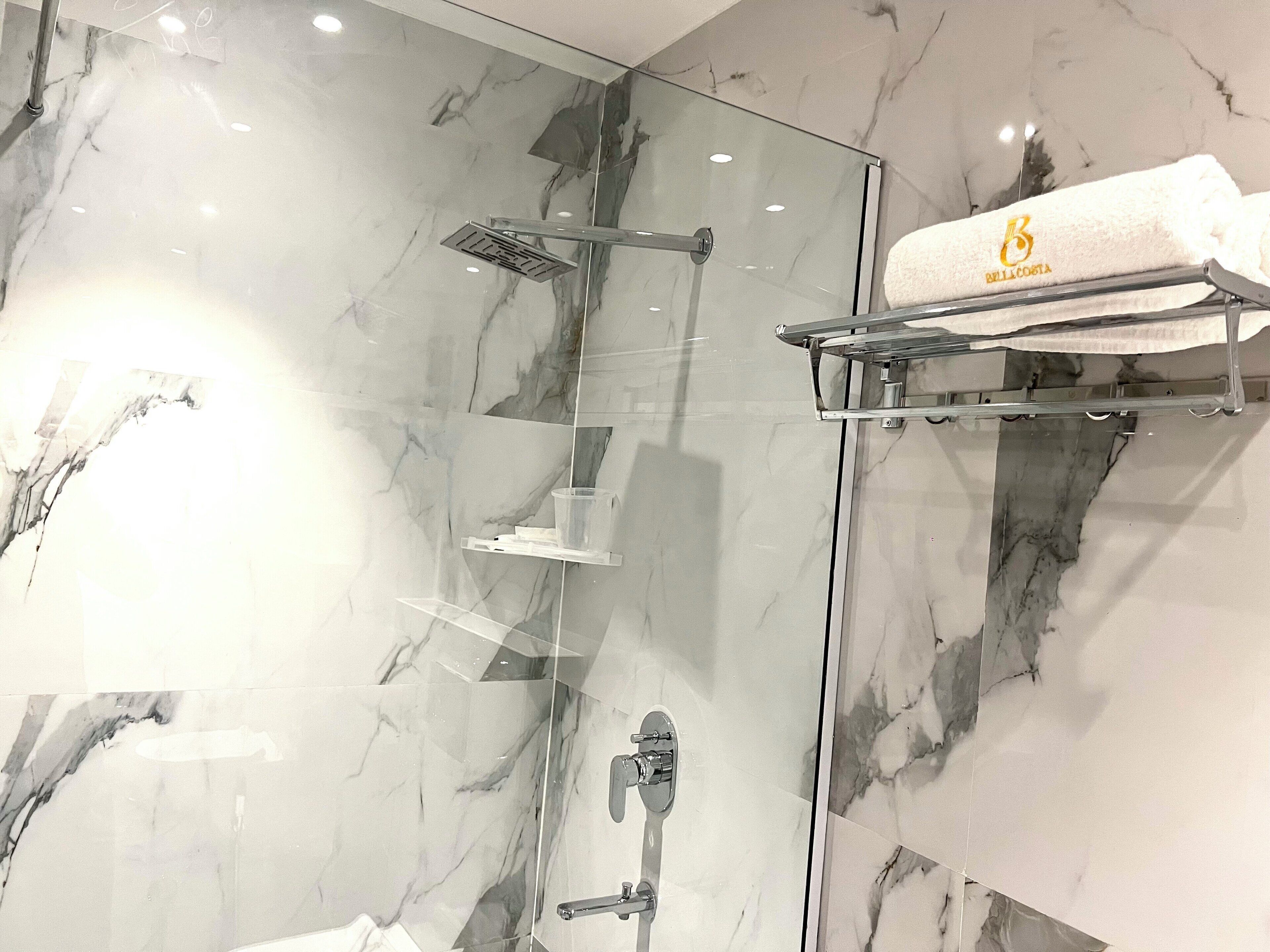 A modern bathroom with a glass shower enclosure, marble walls, and a towel rack with a branded towel.