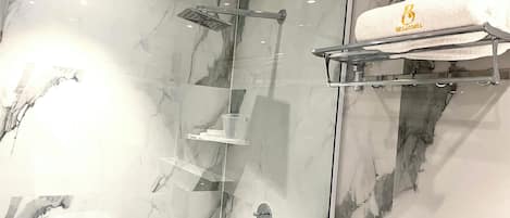 Un baño moderno con cabina de ducha de vidrio, paredes de mármol y un perchero con toalla de la marca.