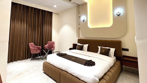 A modern bedroom with a large bed, two chairs, a desk, and a large window with curtains. - Hotel Bella Costa (Ludhiana)