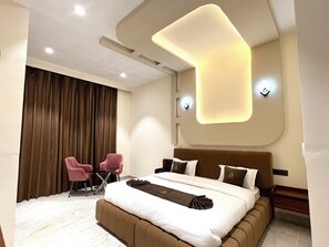 A modern bedroom with a large bed, two chairs, a desk, and a large window with curtains.