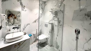 A modern bathroom with a glass-enclosed shower, a white sink, and a marble-tiled wall. - Hotel Bella Costa (Ludhiana)