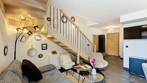 Un salon moderne avec un canapé gris, une petite table ronde ornée d’un vase de fleurs et un escalier doté d’une rampe en bois.