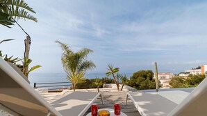 A balcony with two white lounge chairs, a small round table, and a view of the sea and cityscape. - Contemporary house with private pool on Costa Brava (Roses)