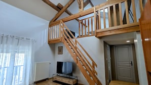 Ein Loft-Zimmer mit freiliegenden Holzbalken, einer Holztreppe, einem Flachbildfernseher und einer Heizung.