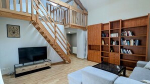 Ein großzügiger Wohnbereich mit einer Holztreppe, einem Fernseher, einem Bücherregal und einem Sofa.