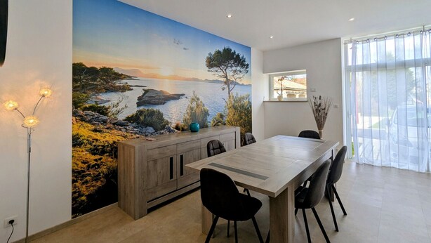 Ein Essbereich mit einer großen Wandmalerei einer Küstenlandschaft, einem Holztisch und schwarzen Stühlen.