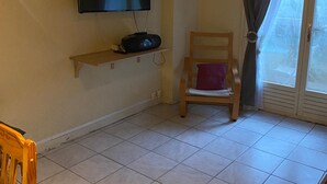 Un salon avec un téléviseur à écran plat fixé au mur, un fauteuil en bois avec un coussin et une fenêtre avec des rideaux.
