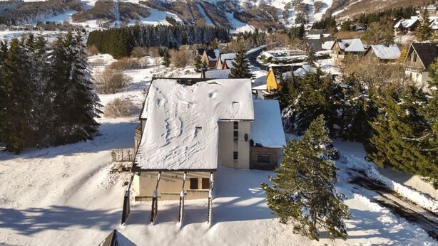 Un village enneigé, avec des maisons traditionnelles, une église et des montagnes en arrière-plan.