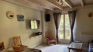 Un salon chaleureux avec une table en bois, un téléviseur, une radio et un fauteuil confortable.
