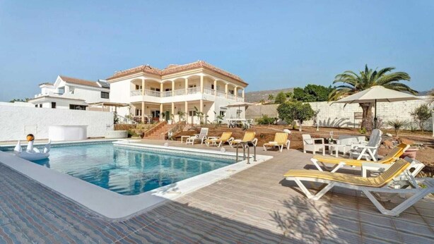 A pool area with lounge chairs and a building with a tiled roof. - Villa Luxury el Mirador (Adeje)