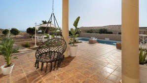 A covered outdoor area with a hanging chair, potted plants, and a swimming pool. - Villa Luxury el Mirador (Adeje)