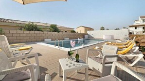 A rooftop pool area with lounge chairs and a table, surrounded by a low stone wall and buildings in the background. - Villa Luxury el Mirador (Adeje)
