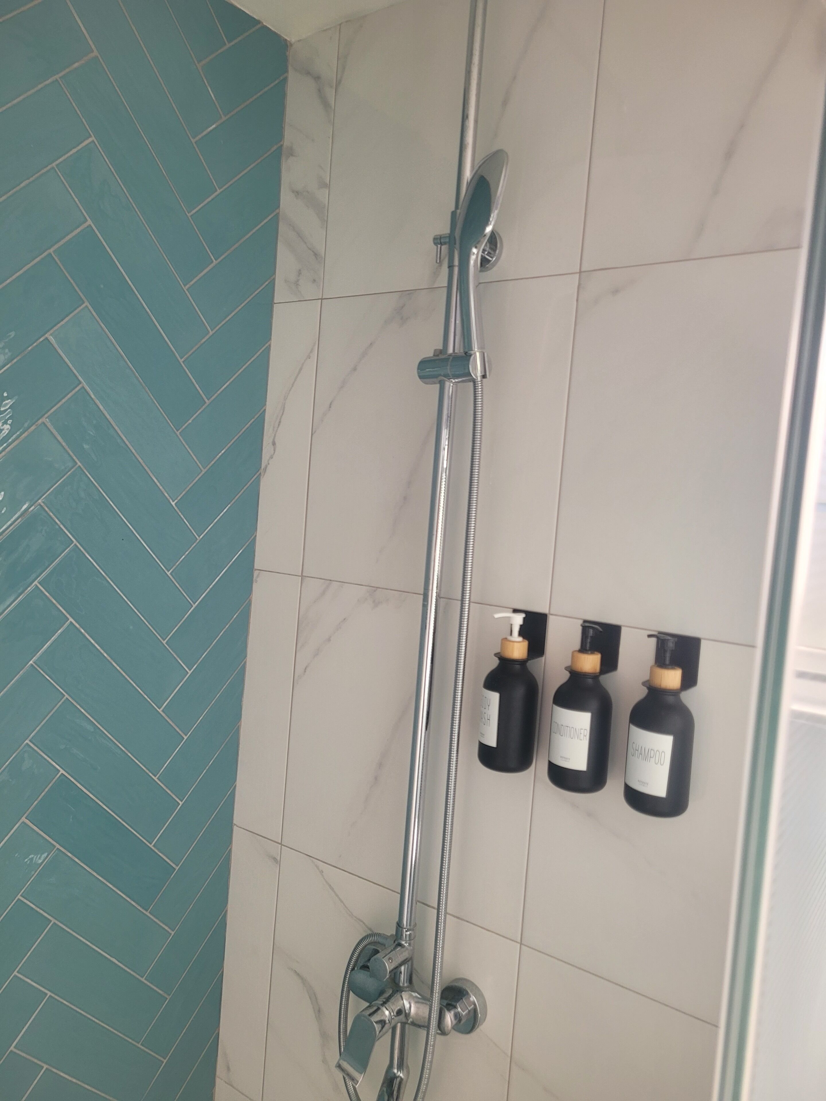 A shower area with a glass door, a handheld showerhead, and two bottles of shampoo and conditioner on the wall.