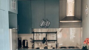 A compact kitchen with grey cabinets, a built-in stove, and a small dining area with a bench. - Modern Grenada Studio with Mountain Views & Free Parking (Saint George's)