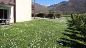 A modern building with a balcony, a grassy lawn with white flowers, and a mountainous backdrop. - Modern 51m² Apartment in Luchon - 4 pers, Terrace, Parking (Bagnères-de-Luchon)