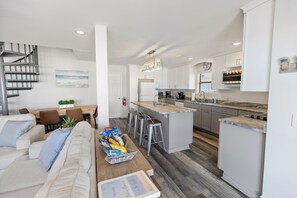 Una cocina moderna con armarios blancos, una isla central y un comedor con sofá y sillas.
