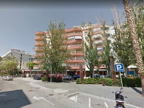 Un hôtel à plusieurs étages doté de balcons, un panneau indiquant un parking et une rue bordée de voitures garées.