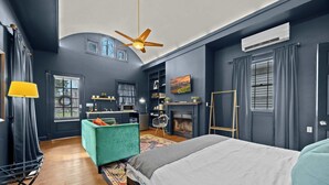 Un dormitorio moderno con una cama grande, ventilador de techo, chimenea y vistas al exterior a través de una ventana.
