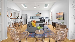 Una sala de estar moderna con un sofá gris, sillones de mimbre, una mesa de centro y un televisor.