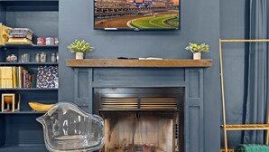 A modern living room with a fireplace, a television mounted above it, and a wooden shelf with decorative items.