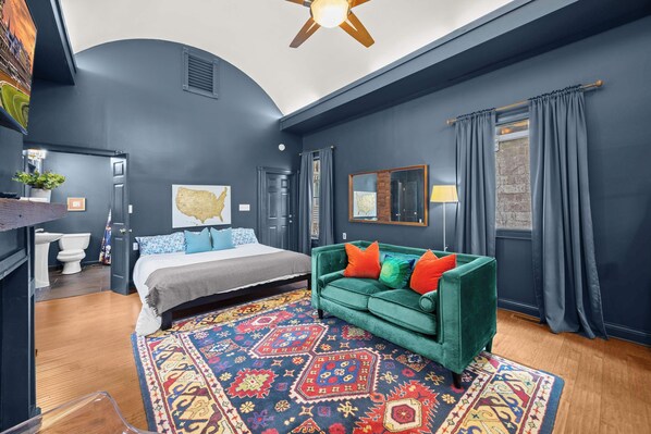 Une chambre à coucher avec un lit, un canapé vert, un tapis à motifs et un ventilateur de plafond.