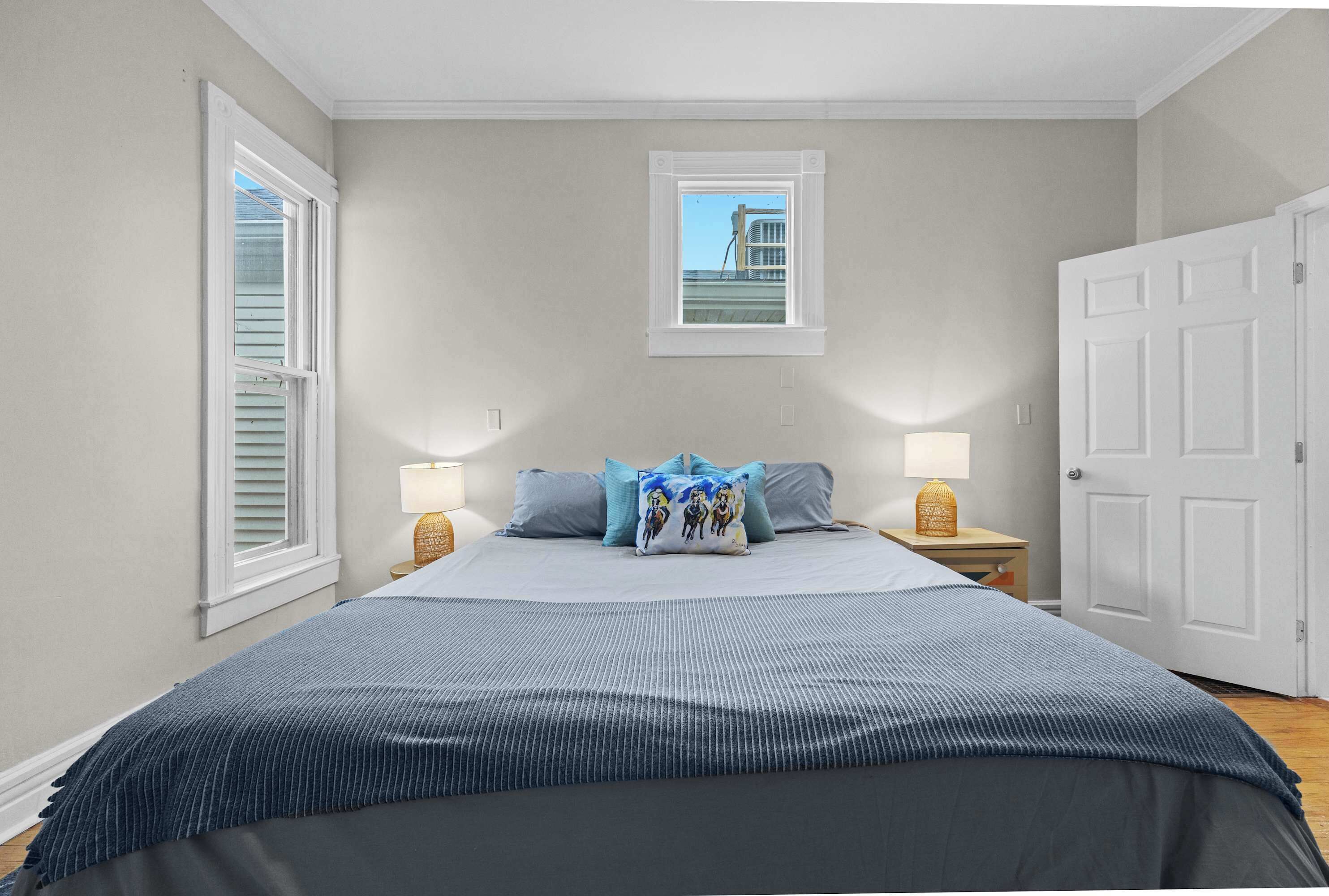 A bedroom with a large bed, two bedside tables with lamps, a window with blinds, and a door.