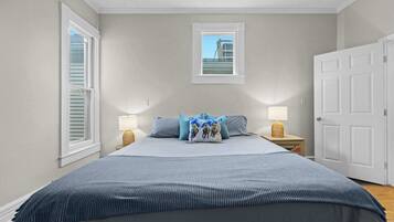 A bedroom with a large bed, two bedside tables with lamps, a window with blinds, and a door.