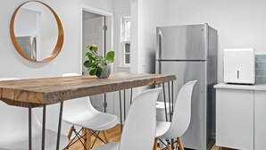 Een moderne keuken met een houten eettafel, witte stoelen, een roestvrijstalen koelkast en een wit kastje.