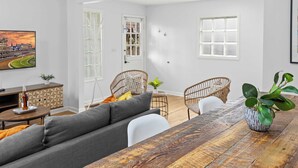 Een moderne woonkamer met een grijze bank, een houten eettafel, rieten stoelen en een potplant.
