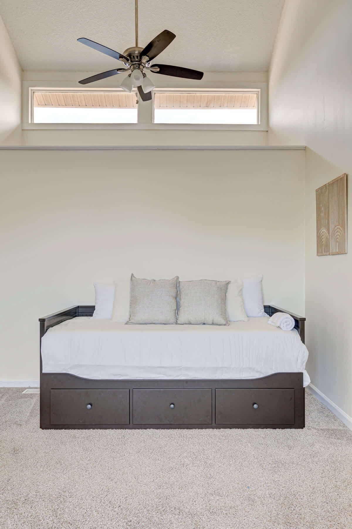 A bedroom with a bed, ceiling fan, and two windows.
