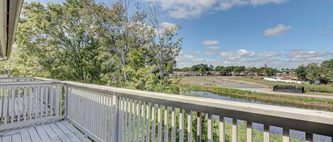 A wooden deck with a railing overlooking a river and a residential area.