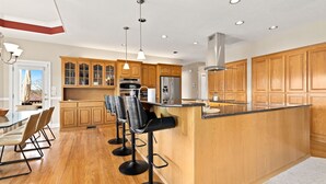 Une cuisine moderne avec des meubles en bois, un îlot central doté de tabourets de bar, des appareils en acier inoxydable et un éclairage suspendu.