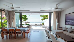 A spacious living area with a dining set, a sofa, and a large window offering a view of the ocean.