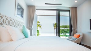 A modern hotel room with a large bed, a chair, and a view of palm trees and the ocean.