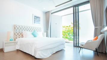 Ein modernes Hotelzimmer mit einem großen Bett, einem weißen Nachttisch, einem Sessel und Blick ins Grüne durch die Glastür.