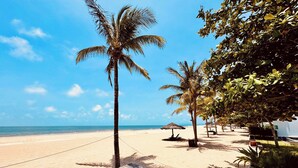 A wooden deck leading to a beach with palm trees and a clear blue sky.