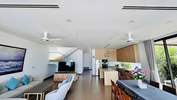 Un espacio habitable moderno con sofá, sillas, una mesa de comedor, una zona de cocina y una escalera que conduce a un nivel superior.